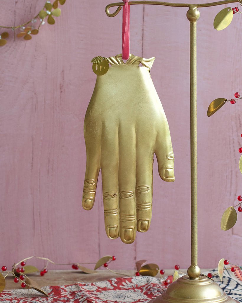 Gold hand-shaped umbrella stand on a pink surface with decorative elements