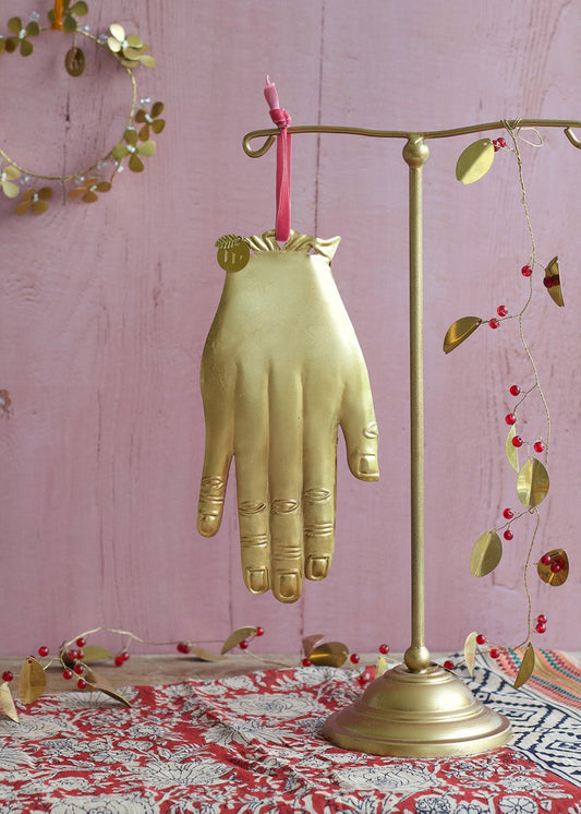 Gold hand-shaped umbrella stand on a pink surface with decorative elements