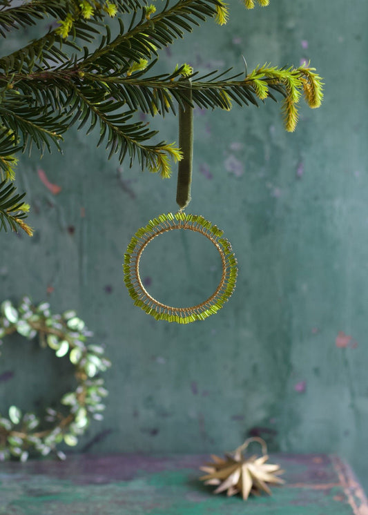 Handmade light green beaded ornament with golden wire and velvet ribbon hanging on a Christmas tree.