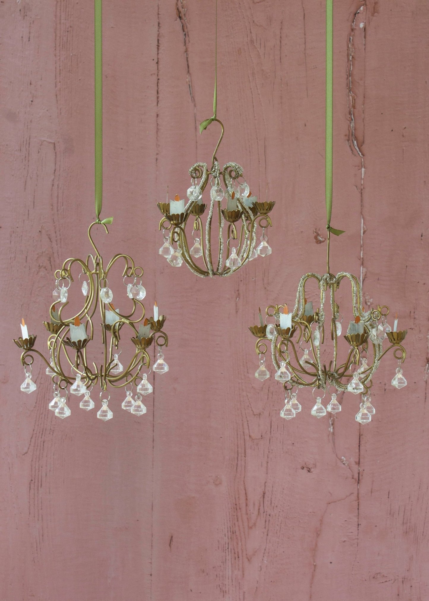 Three small chandeliers hanging against a pink wall