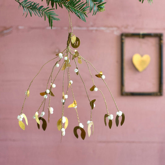 Decorative mistletoe with gold leaves and white berries hanging against a pink wall.