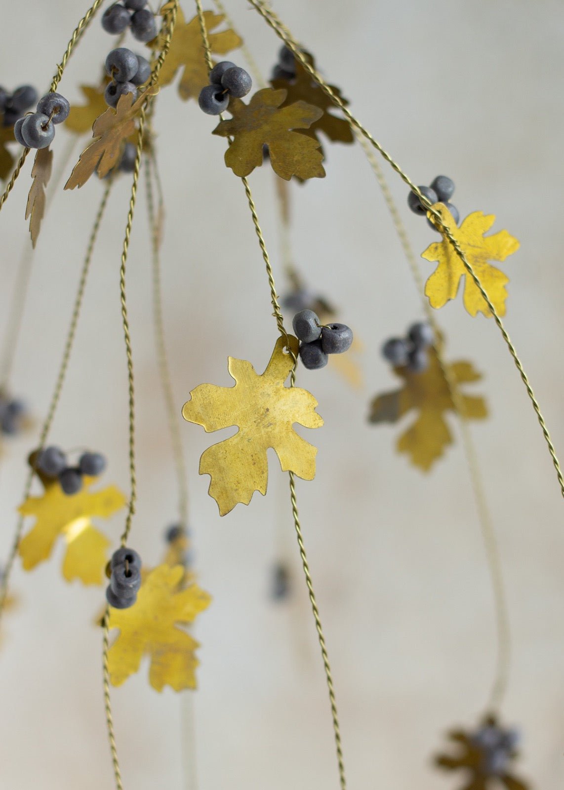Close-up of brass oak leaves and grey beads hanging from twisted brass wire strands.