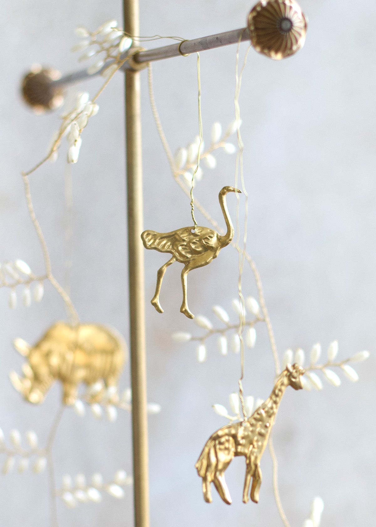 Brass ostrich and giraffe ornaments hanging from fine wire, with a golden rhinoceros visible in the background.