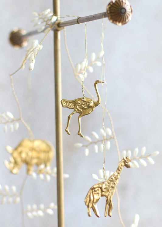 Brass ostrich and giraffe ornaments hanging from fine wire, with a golden rhinoceros visible in the background.