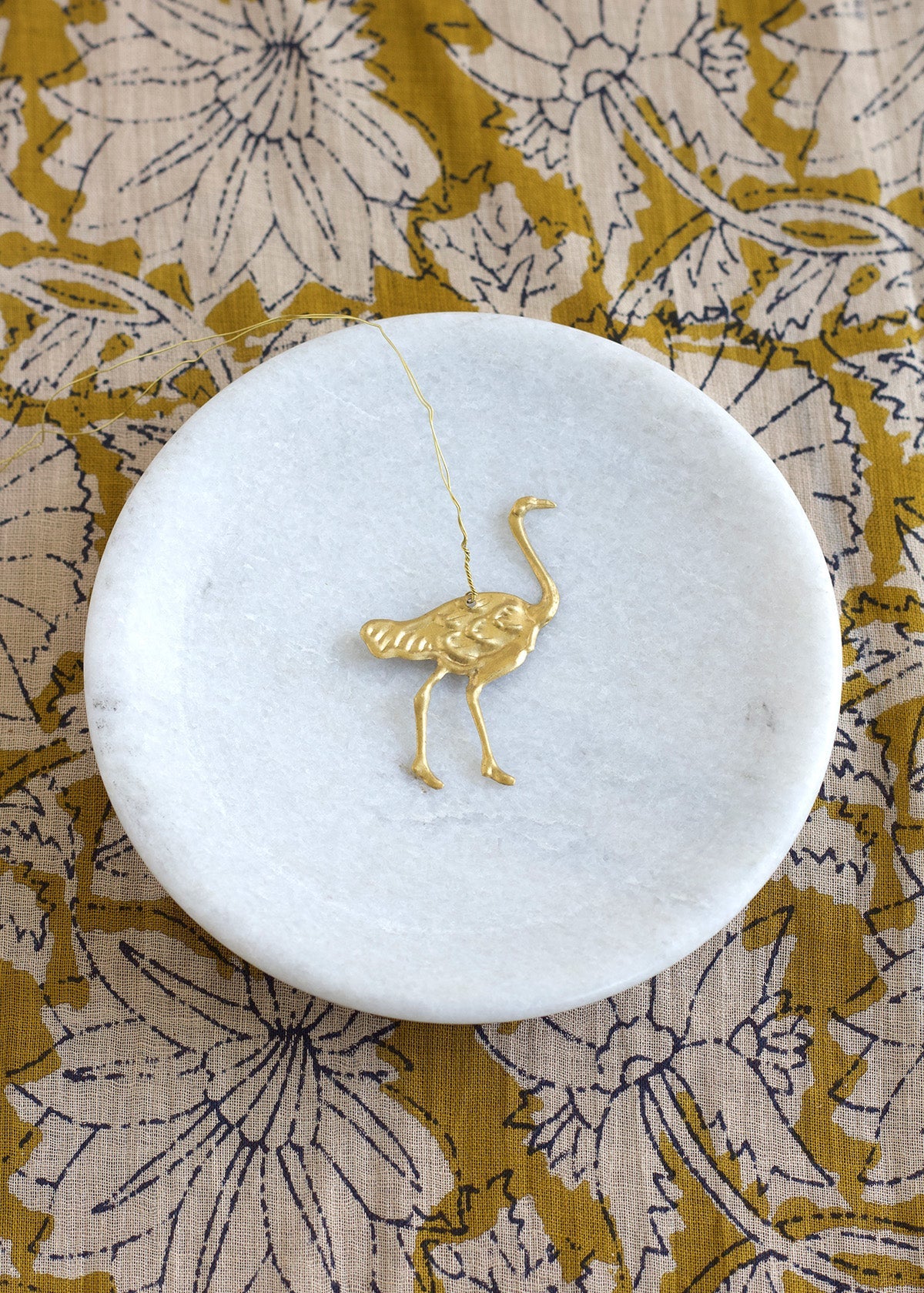 Gold ostrich pendant on a white marble coaster with a floral patterned fabric background