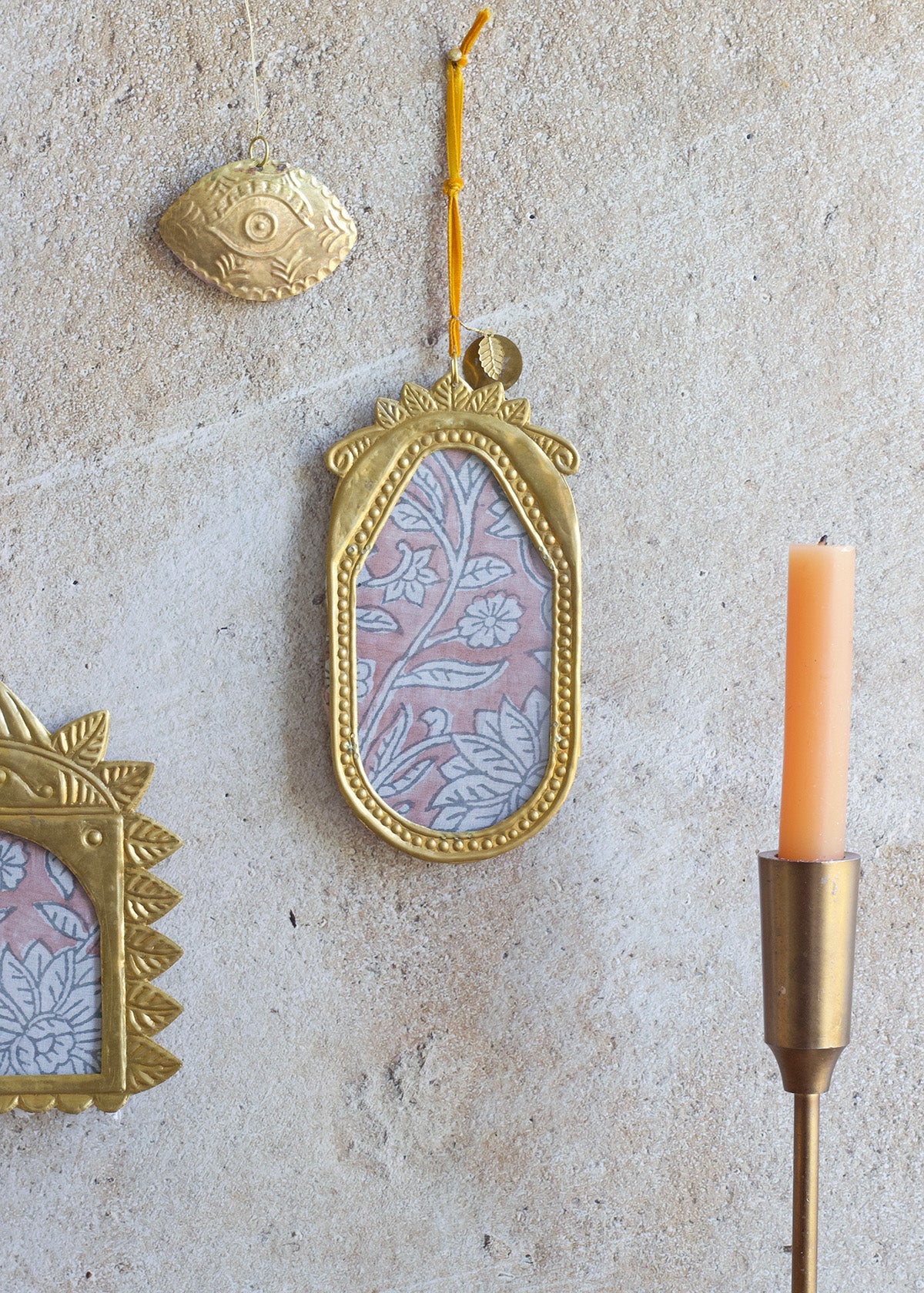 Decorative gold frame with floral design on a textured wall with a candle and other decorative items.