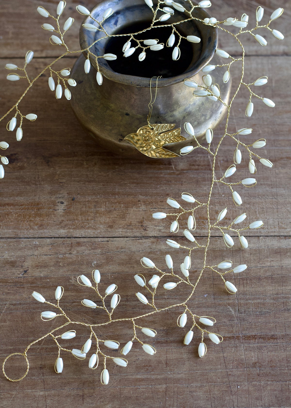 Decorative white beads on gold thread with a ceramic bowl on a wooden surface