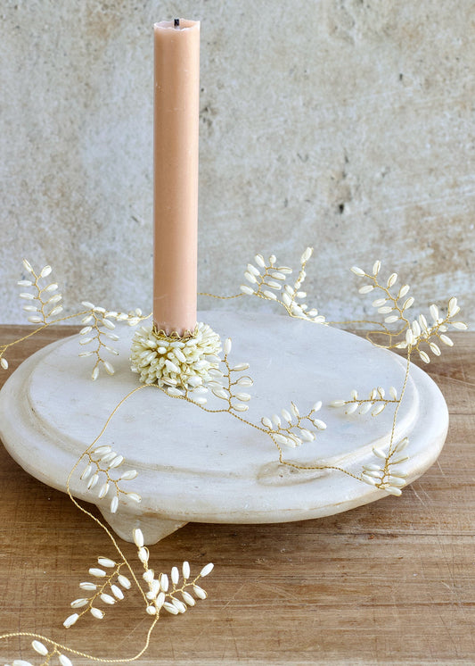 Candle on a marble holder with decorative branches against a textured wall.