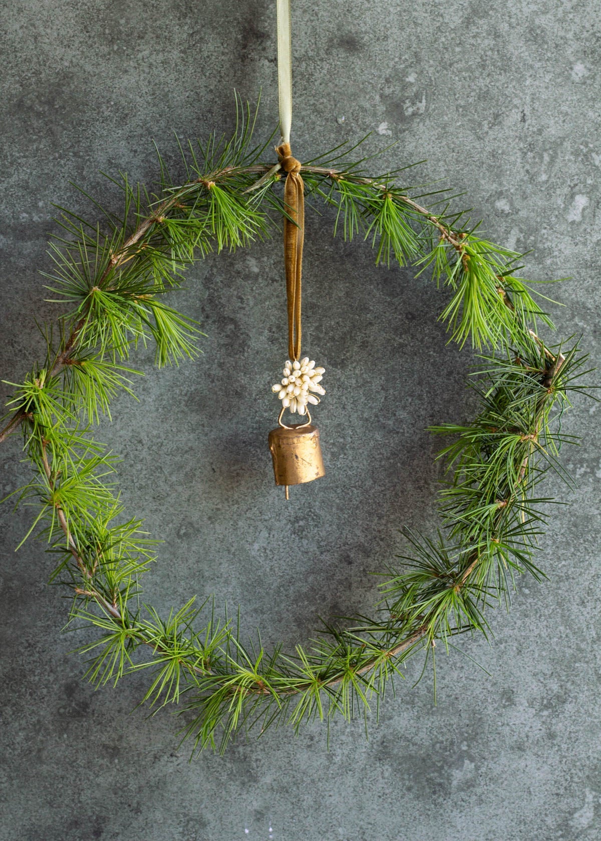Green wreath with a gold bell and white flower on a gray background