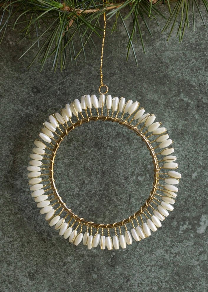 Decorative wreath ornament with beads hanging on a branch.