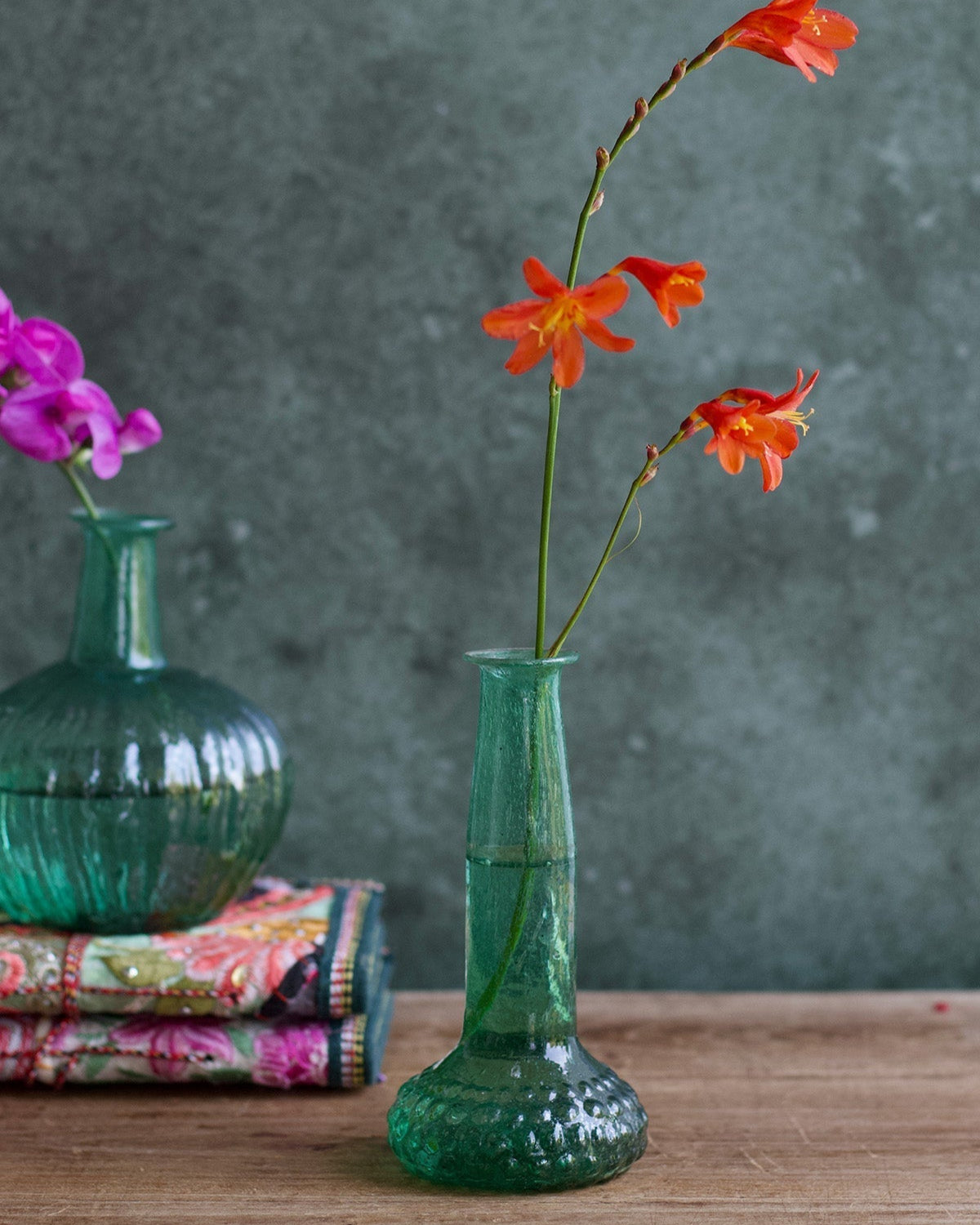 Green textured vase with orange flowers on a wooden surface against a gray background