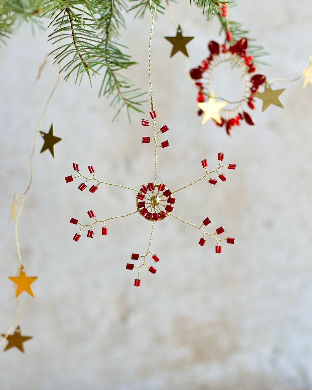 Handmade red and gold beaded snowflake ornament hanging in a Christmas tree.