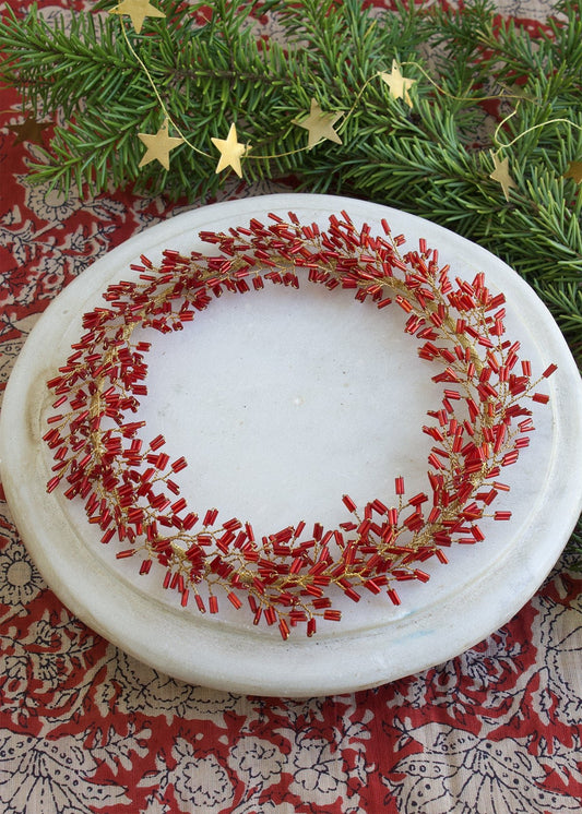 Decorative plate with red and gold wreath design on a patterned surface with greenery and stars.