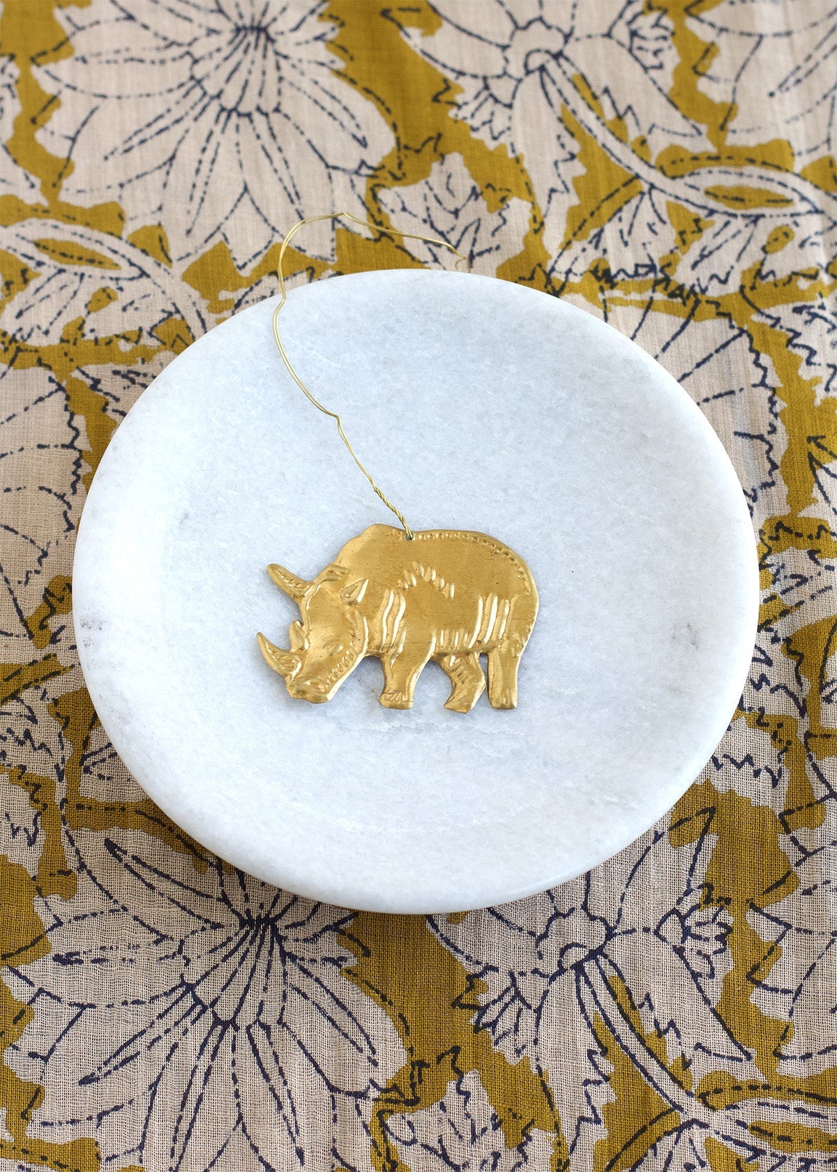Gold rhinoceros pendant on a white marble coaster with a floral patterned fabric background