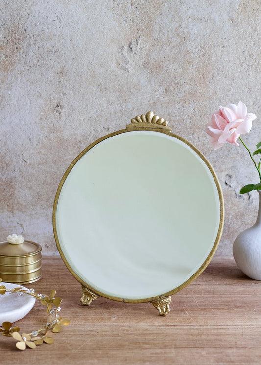 Decorative round mirror with gold frame on a wooden surface with a neutral background