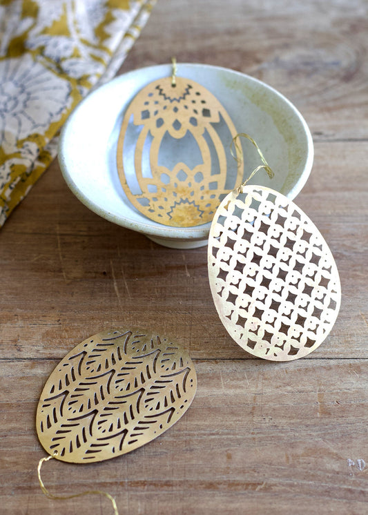 Gold earrings with intricate patterns on a wooden surface.