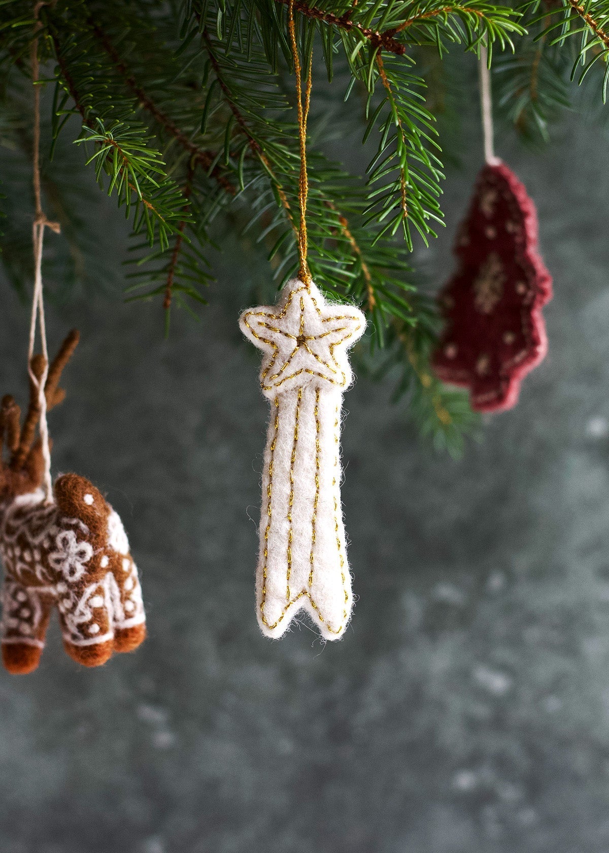 Handmade white felt Christmas ornament shaped like a falling star with golden embroidery, hanging in a Christmas tree.