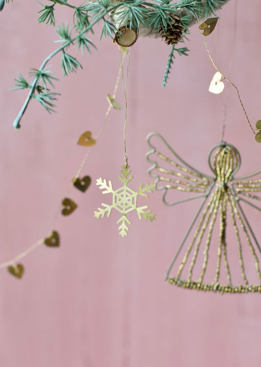 Golden brass snowflake ornament with cut-out details, hanging from a branch.