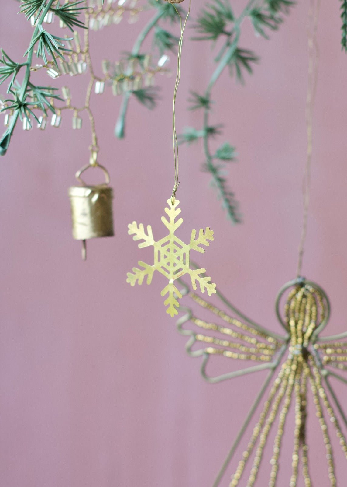 Golden brass snowflake ornament with cut-out details, hanging from a branch.