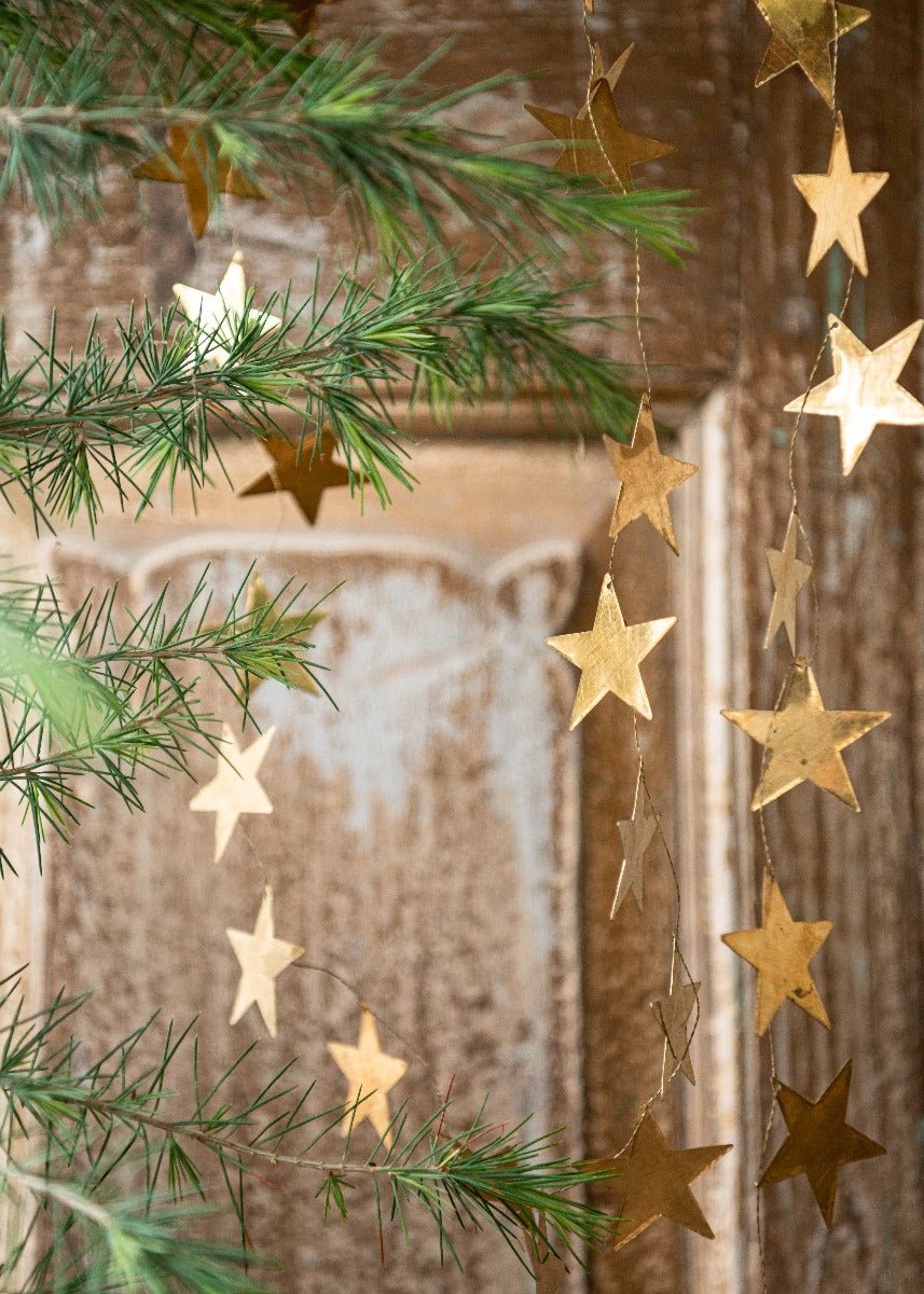 Golden metal star garland hanging between pine branches and in front of a rustic wooden door, creating a festive and warm holiday atmosphere.