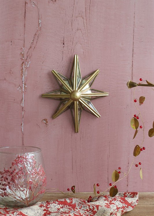 Small mirrored star wall decoration with brass edging, hanging on a pink wooden wall, styled with red berry garland and a glass candle holder.