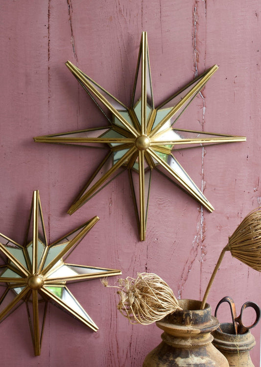 Two mirrored star wall decorations with gold brass edging, mounted on a pink wooden wall and styled with rustic pottery and dried botanicals.