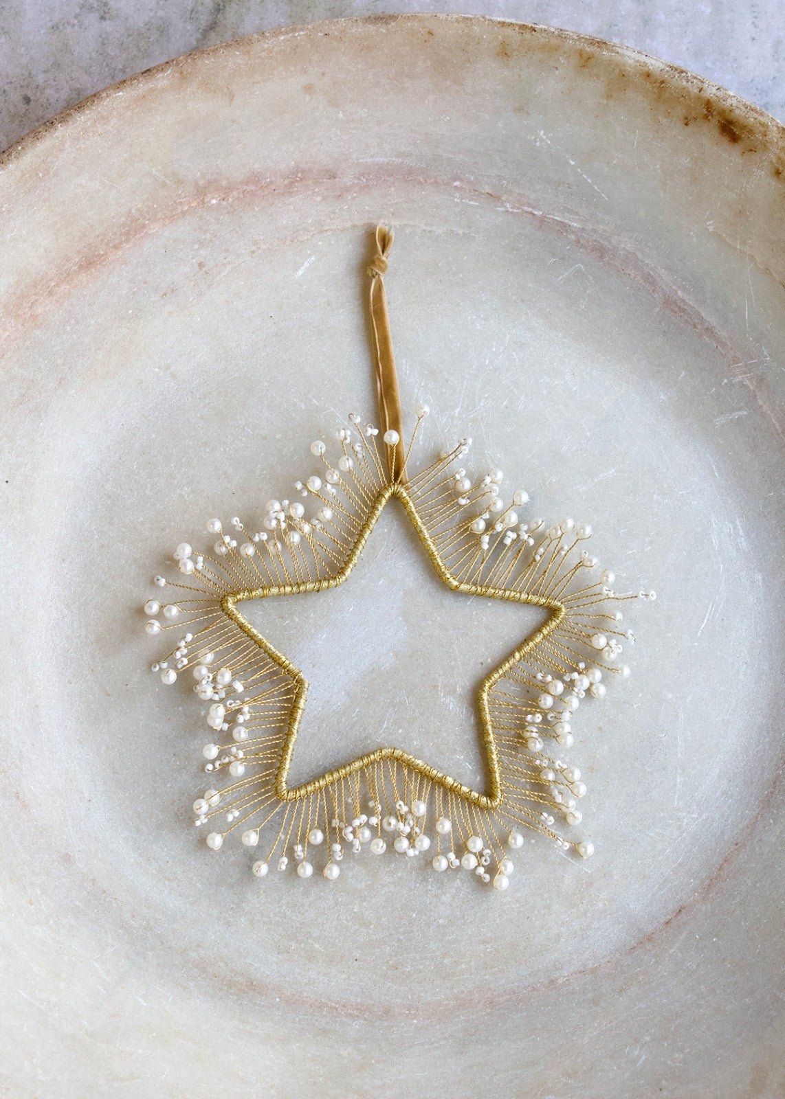 Gold-colored star adorned with white pearls, suspended on a soft velvet cord.