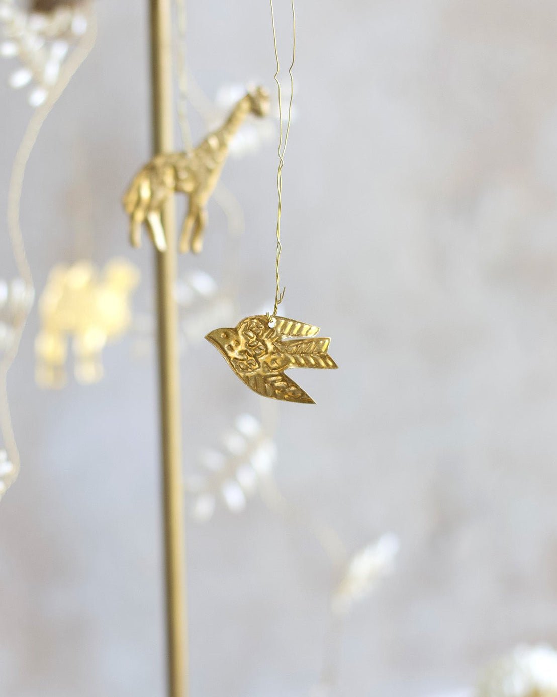 Gold bird ornament hanging from a string with blurred lights in the background