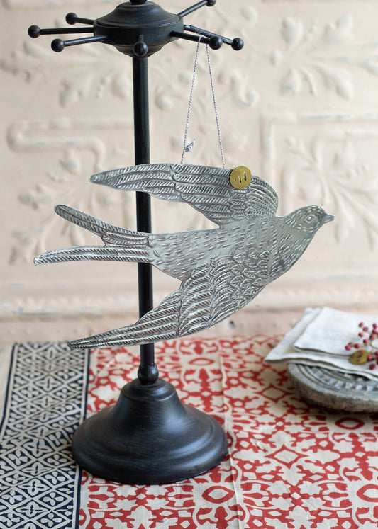 Zinc bird ornament with embossed detailing, hanging from a black metal stand.