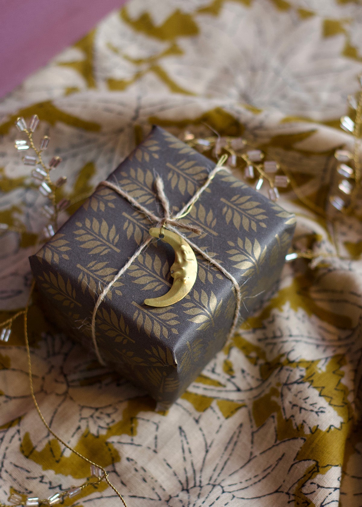 Gift box with floral pattern and gold crescent moon charm on a floral fabric background