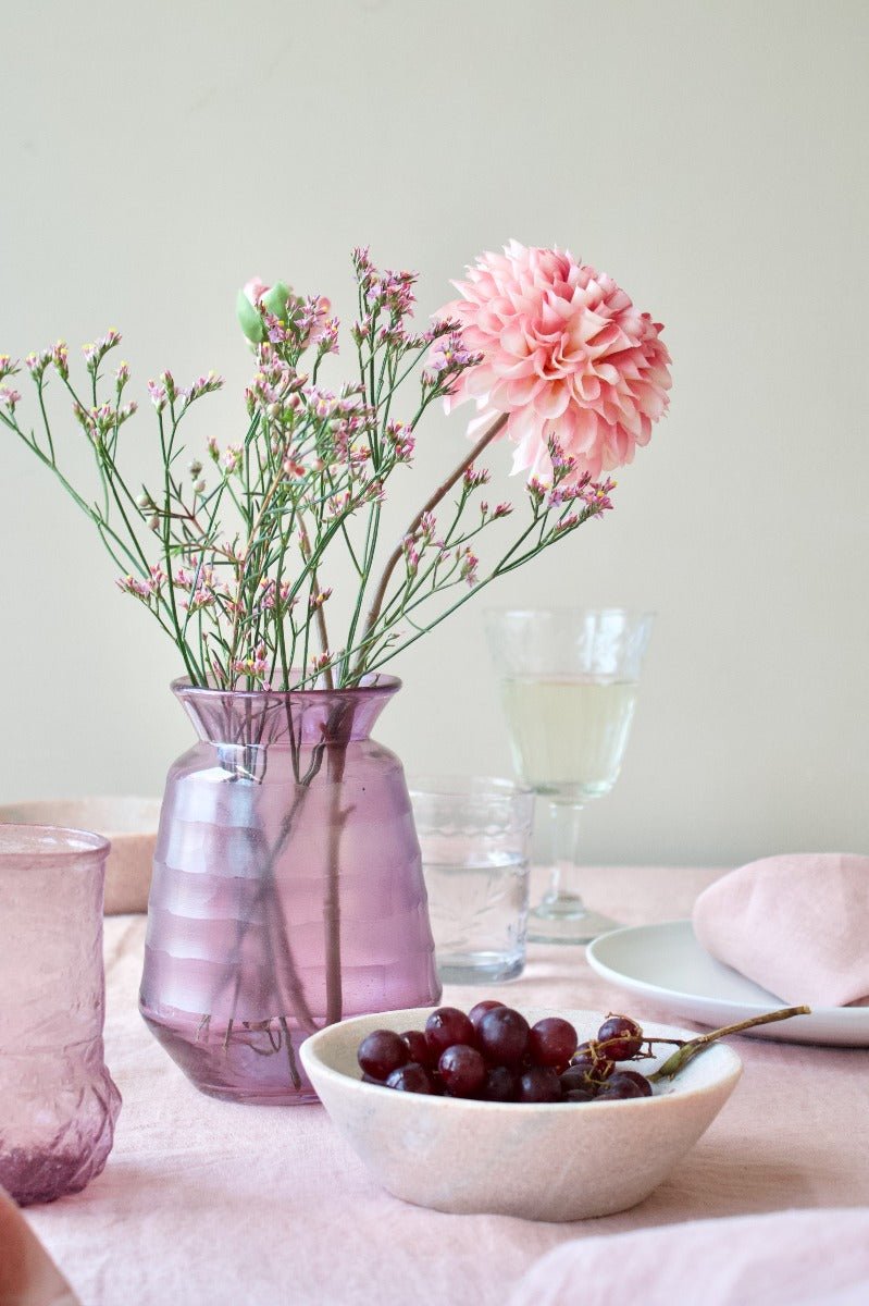 Lilac ribbed glass vase with a flared rim, filled with pink and white flowers on a softly styled table setting.