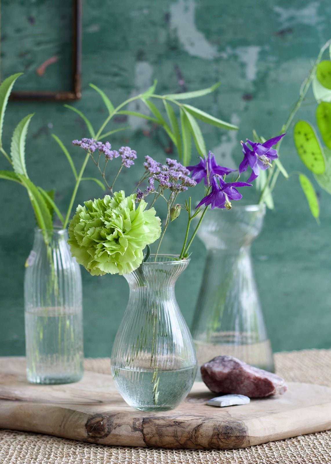 Bulb-shaped ribbed glass vase with flared rim, styled with green and purple wildflowers on a wooden board.
