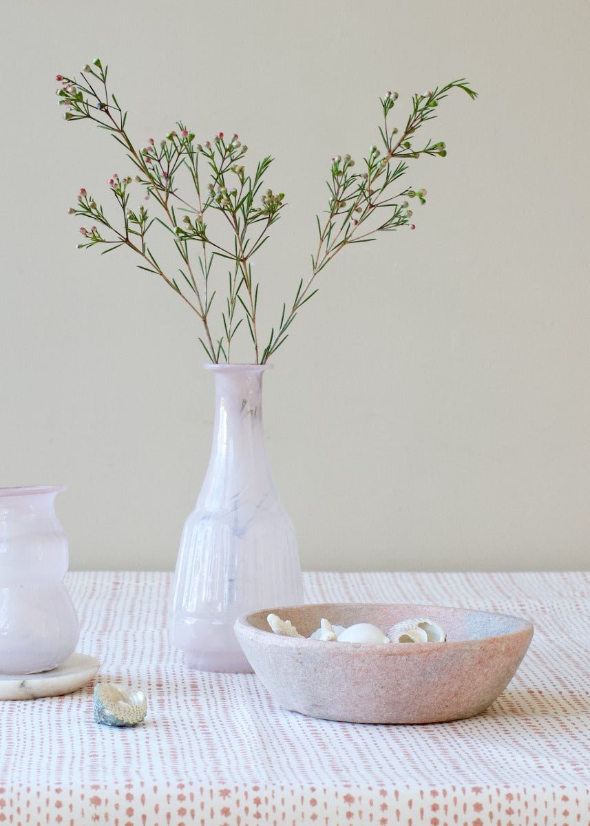 Tall opaline glass vase in soft white with subtle marbled veining, styled with delicate green branches on a patterned tablecloth.