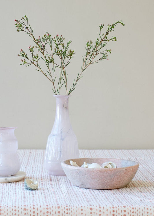 Tall opaline glass vase in soft white with subtle marbled veining, styled with delicate green branches on a patterned tablecloth.