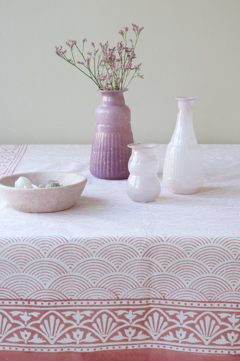Three opaline glass vases in soft pink and white tones, displayed on a patterned tablecloth with delicate flowers and a natural stone bowl.