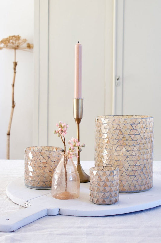Large mosaic glass vase with soft peach and ivory triangle pattern, styled with matching candle holders and pink floral accents.
