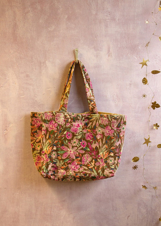 Handcrafted velvet tote bag with pink floral embroidery hanging against a soft pastel wall.