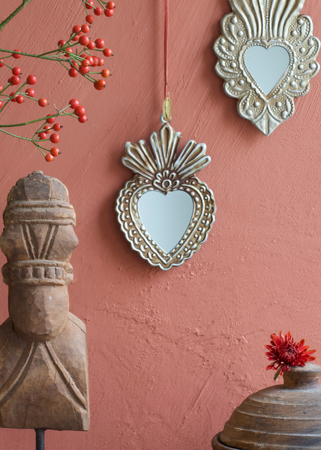Decorative heart-shaped mirrors on a pink wall with a wooden sculpture and red flowers.