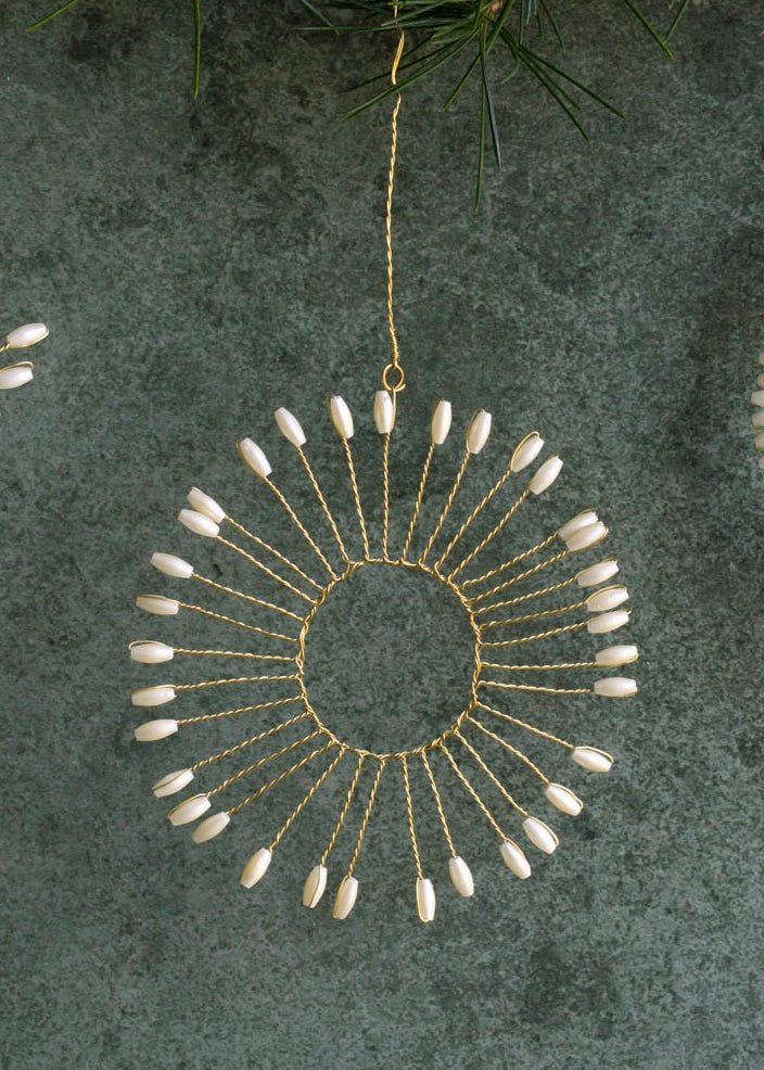 Decorative hanging ornament with gold wire and white beads on a textured green background