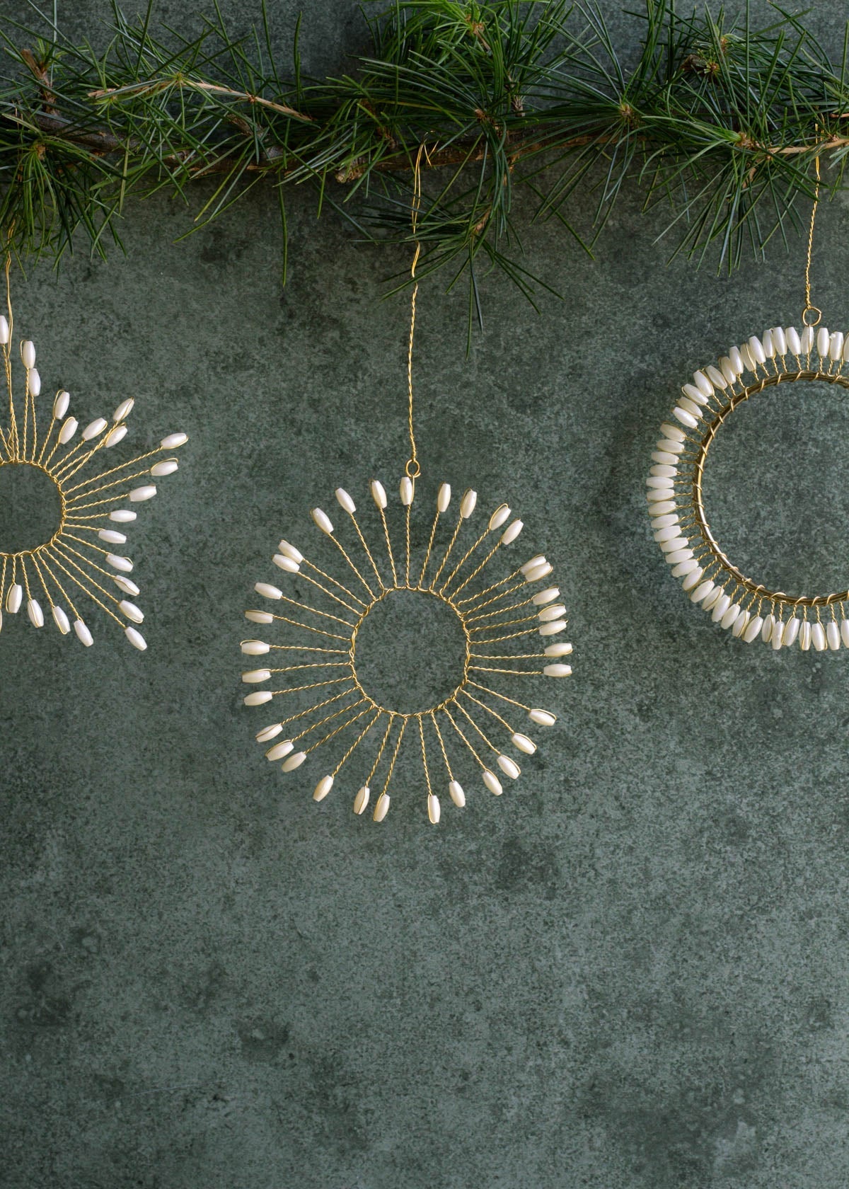 Decorative circular ornaments with white beads on a textured green surface with pine branches.