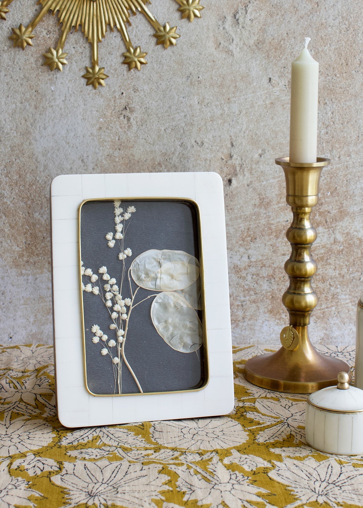 White photo frame with floral design on a textured surface with a candle and decorative item.