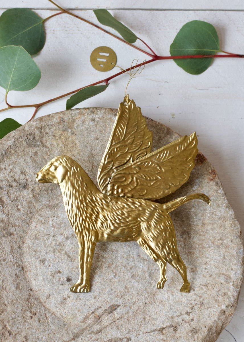Gold brass winged dog ornament lying on a natural stone surface with eucalyptus leaves