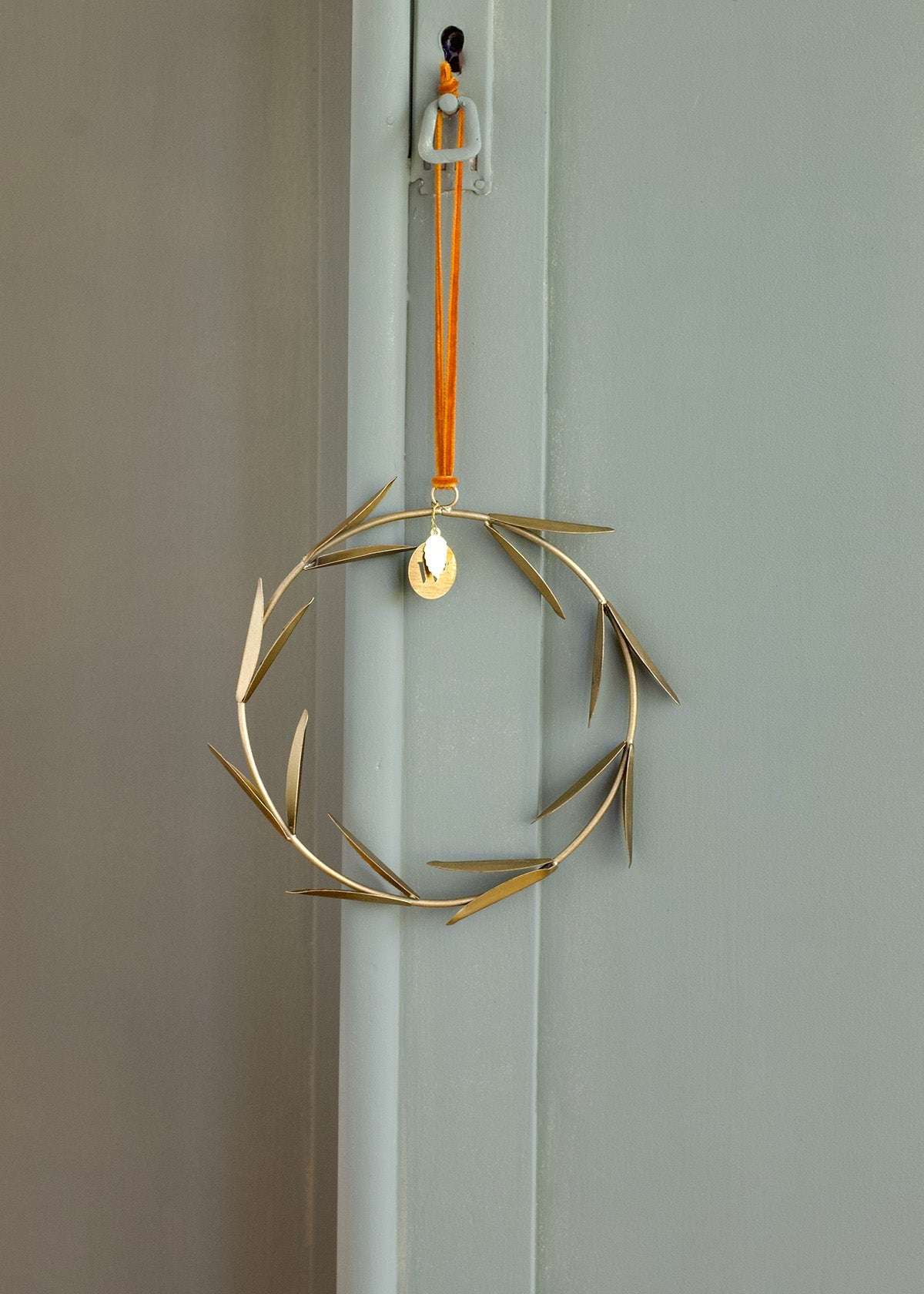 Decorative gold wreath with a orange velvet string hanging on a door