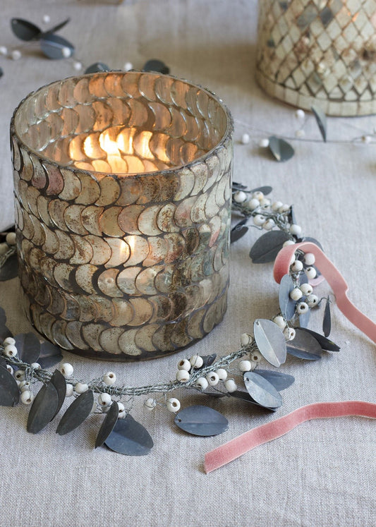 Decorative candle holder with a lit candle on a textured surface with floral and ribbon accents.