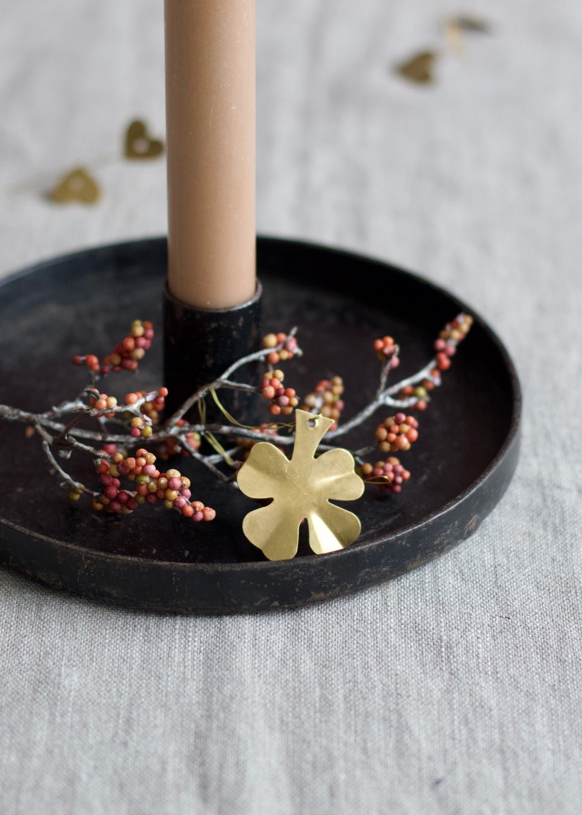Brass four-leaf clover ornament displayed on a candle tray with berries and a beige taper candle.
