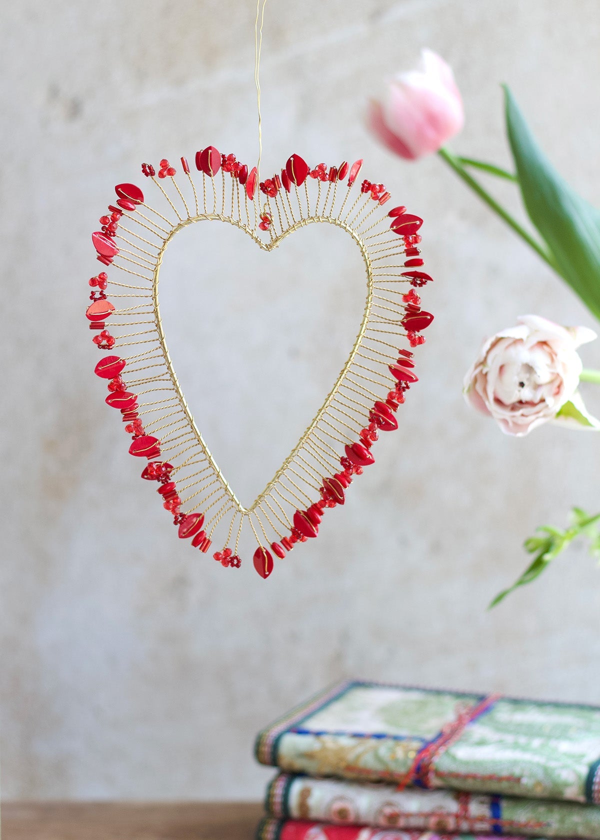 A decorative red heart-shaped halo hanging against a neutral background with a floral patterned object to the side.