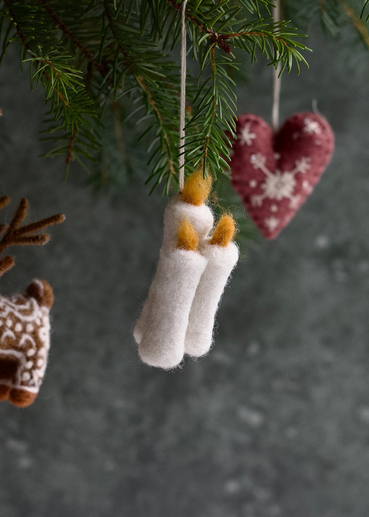 Felted Christmas ornaments including a heart, deer, and candles hanging from a tree.