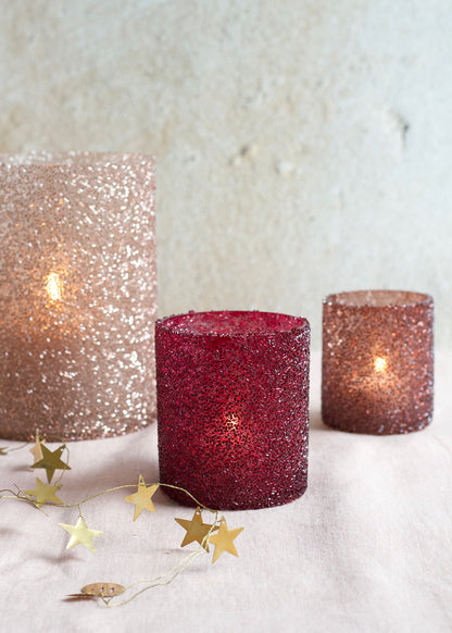 Three glittery candles on a textured surface with gold star decorations.