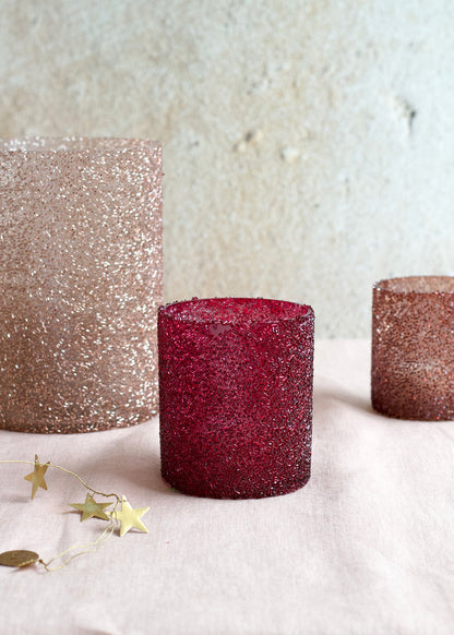 Three glittery candles in rose gold, red, and bronze on a light background.