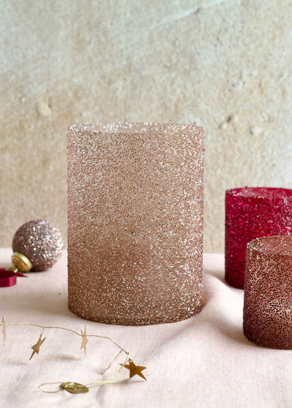 Glittery cylindrical candles on a textured surface with decorative elements.